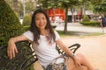 Young beautiful and happy Asian woman on park bench - lifestyle portrait of Attractive Japanese girl in Summer dress resting Royalty Free Stock Photo