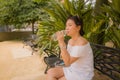 Young beautiful and happy Asian woman on park bench - lifestyle portrait of Attractive Korean girl in Summer dress drinking water Royalty Free Stock Photo