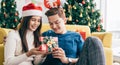 Young beautiful happy Asian woman wearing Santa Claus hat surprises her boyfriend with a Christmas gift at home. Royalty Free Stock Photo