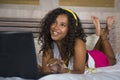 Young beautiful happy black African American woman at home bedroom lying cheerful on bed listening to internet music with headphon Royalty Free Stock Photo