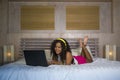 Young beautiful happy black African American woman at home bedroom lying cheerful on bed listening to internet music with headphon