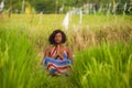 Young beautiful and happy black African American woman sitting at rive field outdoors practicing yoga relaxation and meditation