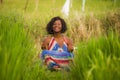 Young beautiful and happy black afro American woman sitting at rive field outdoors practicing yoga relaxation and meditation