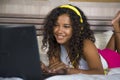 Young beautiful happy black hispanic woman at home bedroom lying cheerful on bed listening to internet music with headphones and l Royalty Free Stock Photo