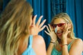 Young beautiful and happy blond woman enjoying shopping trying out clothes and sunglasses in the mirror at vintage and cool beauty Royalty Free Stock Photo