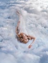 Young beautiful happy blonde woman lies in soft bed on white clouds in sky. Fantasy girl sleeping beauty. Goddess Royalty Free Stock Photo