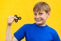 Young beautiful happy boy with freckles blue t-shirt holding fidget spinner on yellow background