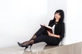 Young Beautiful happy brunette woman holding a notebook dressed in black business suit sitting on a floor in office, smiling, Royalty Free Stock Photo