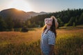 Young beautiful happy cheerful woman in a hat enjoying the sunset in a meadow with mountains view Royalty Free Stock Photo