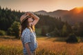 Young beautiful happy cheerful woman in a hat enjoying the sunset in a meadow with mountains view Royalty Free Stock Photo
