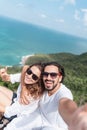 Young beautiful happy couple in sunglasses and white t-shirts on a hilltop overlooking the tropical sea. Vacation, travel, Royalty Free Stock Photo