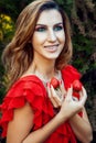 Young beautiful happy funny girl with red dress and makeup holding strawberry in summertime in the park. Royalty Free Stock Photo