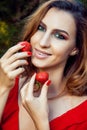 Young beautiful happy funny girl with red dress and makeup holding strawberry in summertime in the park. Royalty Free Stock Photo