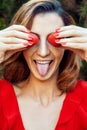 Young beautiful happy funny girl with red dress and makeup holding strawberry in summertime in the park. Royalty Free Stock Photo