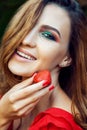 Young beautiful happy funny girl with red dress and makeup holding strawberry in summertime in the park. Royalty Free Stock Photo