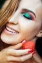 Young beautiful happy funny girl with red dress and makeup holding strawberry in summertime in the park. Royalty Free Stock Photo