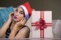 Young beautiful and happy girl in Santa hat holding Christmas present box with ribbon smiling cheerful and excited at home couch r Royalty Free Stock Photo