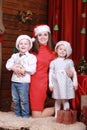 Young beautiful happy mom with little son and daughter in santa`s hats celebrating Christmas and new year at home Royalty Free Stock Photo