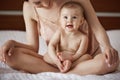 Young beautiful happy mom in sleepwear and her newborn baby sitting on bed in morning smiling playing together. Royalty Free Stock Photo