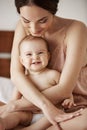 Young beautiful happy mom in sleepwear and her newborn baby sitting on bed smiling playing together at home. Royalty Free Stock Photo