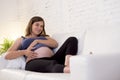 Young beautiful happy 8 or 9 months pregnant woman at home living room couch holding big belly Royalty Free Stock Photo