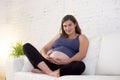 Young beautiful happy 8 or 9 months pregnant woman at home living room couch holding big belly Royalty Free Stock Photo