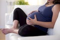 Young beautiful happy 8 or 9 months pregnant woman at home living room couch holding big belly Royalty Free Stock Photo