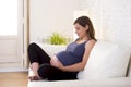 Young beautiful happy 8 or 9 months pregnant woman at home living room couch holding big belly Royalty Free Stock Photo