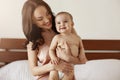 Young beautiful happy mother in sleepwear and her newborn baby sitting on bed in morning smiling playing together. Royalty Free Stock Photo