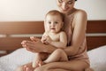 Young beautiful happy mother in sleepwear and her newborn baby sitting on bed in morning smiling playing together. Royalty Free Stock Photo