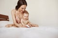 Young beautiful happy mother in sleepwear and her newborn baby sitting on bed in morning smiling playing together. Royalty Free Stock Photo