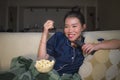 Young beautiful happy and relaxed Asian Chinese woman at home living room sitting cozy on sofa couch watching TV show episode or Royalty Free Stock Photo