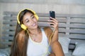 Young beautiful and happy student woman Asian Latin ethnicity mixed listening to music with headphones in bed singing and dancing