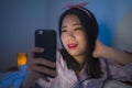 Young beautiful and happy sweet Asian Chinese teen girl with in headband and pajamas enjoying with mobile phone in bed at night