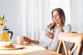 Young beautiful happy woman with blonde long hair in white shirt drinking tea using mobile phone at sunny living room at home Royalty Free Stock Photo