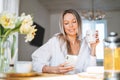 Young beautiful happy woman with blonde long hair in white shirt drinking tea using mobile phone at sunny living room at the home Royalty Free Stock Photo