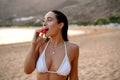 Young beautiful happy woman enjoying sunny day on the beach, eating strawberry. Summer photo. Island girl