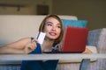 Young beautiful and happy woman at home living room holding credit card using laptop computer for banking and online shopping smil Royalty Free Stock Photo