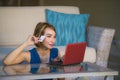 Young beautiful and happy woman at home living room holding credit card using laptop computer for banking and online shopping smil Royalty Free Stock Photo