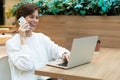 Young beautiful happy woman sitting at a shopping center at a table and working at a computer laptop, using mobile phone Royalty Free Stock Photo