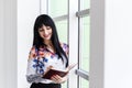 Young Beautiful happy woman standing near the window, writing in notebook, looking to the notebook, smiling Royalty Free Stock Photo