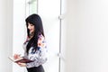 Young Beautiful happy woman standing near the window, writing in notebook, looking to the notebook, smiling Royalty Free Stock Photo