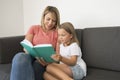 Young beautiful and happy women sitting together with her adorable 7 years old adorable blond girl reading book enjoying telling s Royalty Free Stock Photo