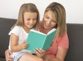 Young beautiful and happy women sitting together with her adorable 7 years old adorable blond girl reading book enjoying telling s Royalty Free Stock Photo