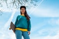 A young beautiful hipster woman poses with a skateboard in her hands. Blue sky in the background. Bottom view. Copy space. Concept