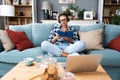 Young beautiful hipster woman sitting on sofa at home listening music on wireless headset and reading a book. Freelance female Royalty Free Stock Photo