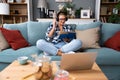 Young beautiful hipster woman sitting on sofa at home listening music on wireless headset and reading a book. Freelance female Royalty Free Stock Photo