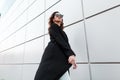 Young beautiful hipster woman in a vintage long black coat in fashionable sunglasses goes on a warm spring day