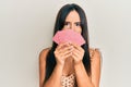 Young beautiful hispanic girl covering face with cards in shock face, looking skeptical and sarcastic, surprised with open mouth Royalty Free Stock Photo