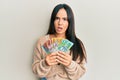 Young beautiful hispanic girl holding australian dollars in shock face, looking skeptical and sarcastic, surprised with open mouth Royalty Free Stock Photo